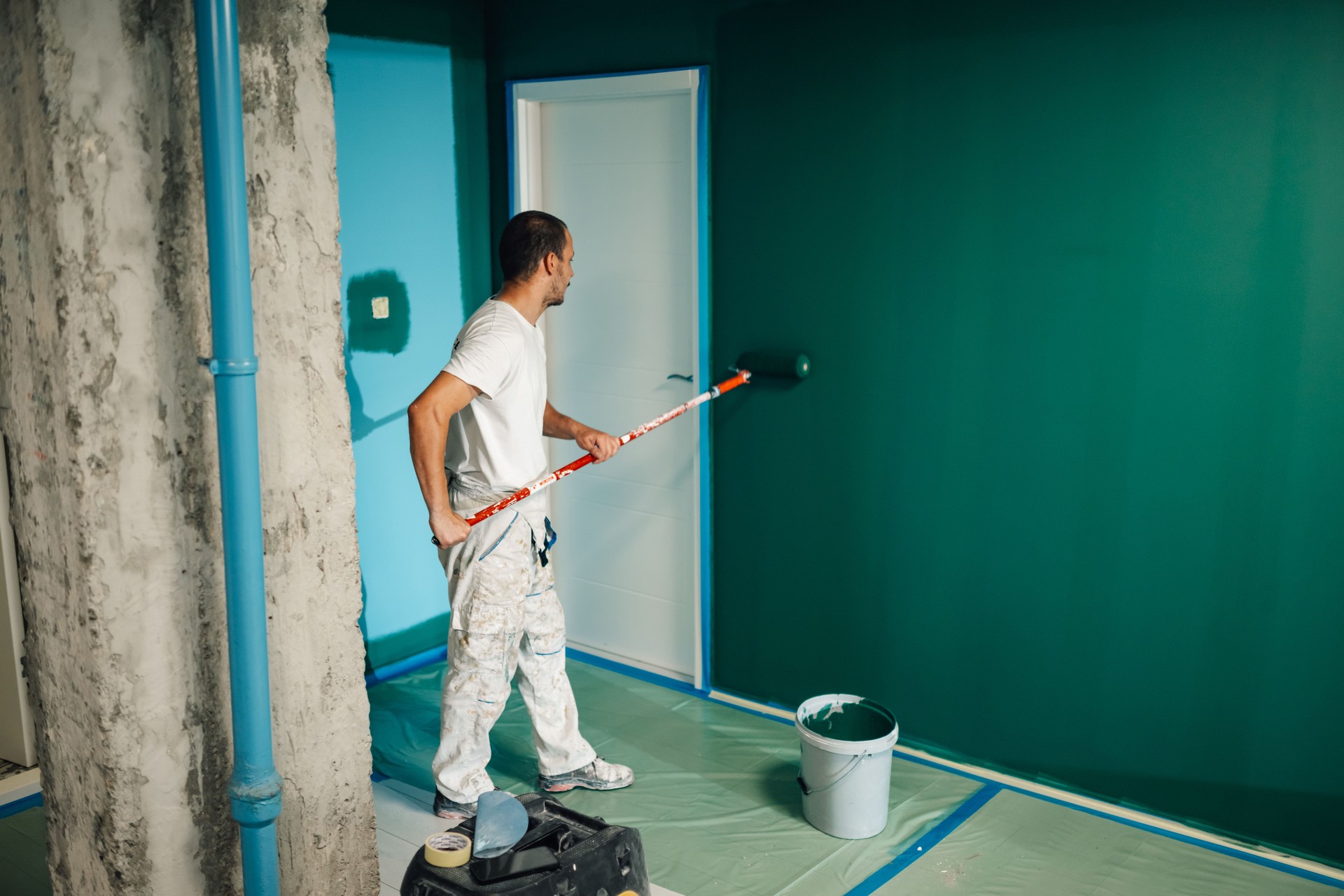Painter painting a wall with a paint roller in a room being renovated