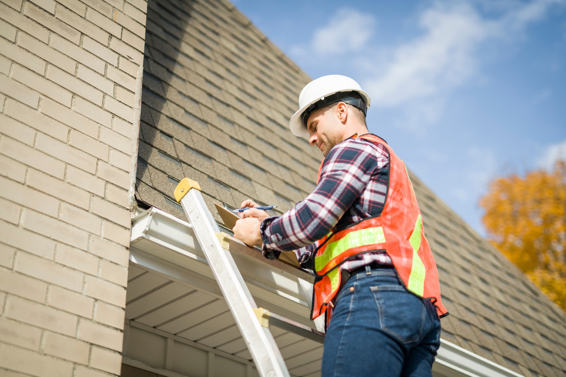 man with hard hat standing on steps inspecting house roof